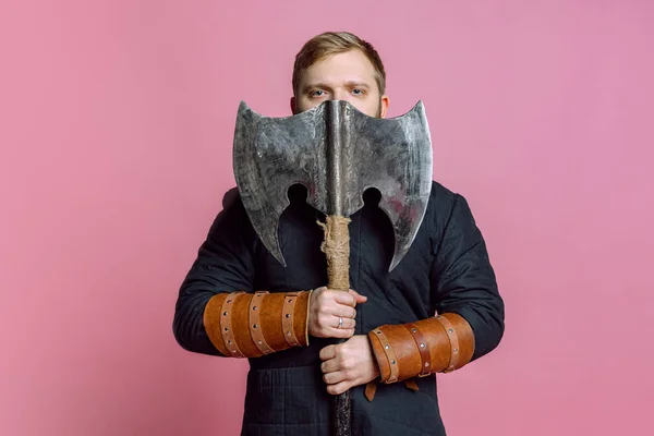 中世の戦士をイメージした若い髭を生やした男のスタジオショット、ピンクの背景に斧で隔離された鎖鎧の弓。時代の比較 — ストック写真