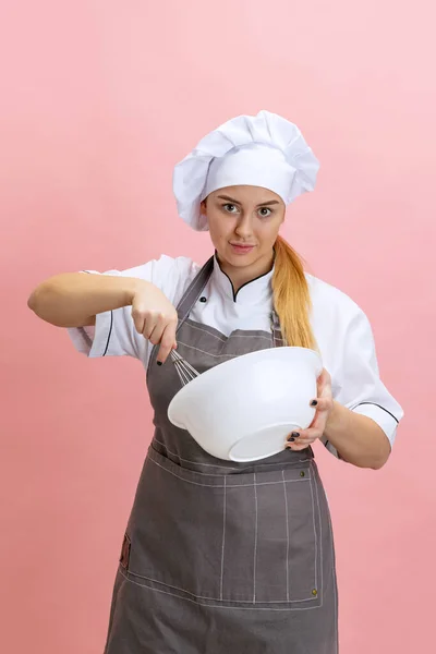 Junge lächelnde Frau, Köchin, Köchin in weißer Uniform, die isoliert auf rosa Hintergrund kocht. Küche, Beruf, Geschäft, Essen, Geschmack, Restaurantkonzept. — Stockfoto