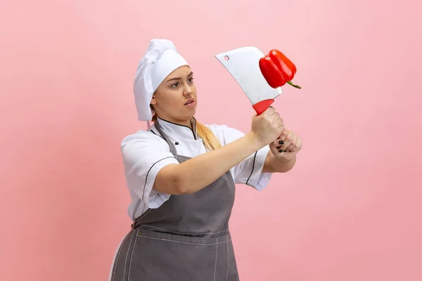 Комический портрет женщины-повара, шеф-повара в белой шляпе и кухонном фартуке на розовом фоне. Кухня, профессия, бизнес, еда, вкус, концепция ресторана. — стоковое фото