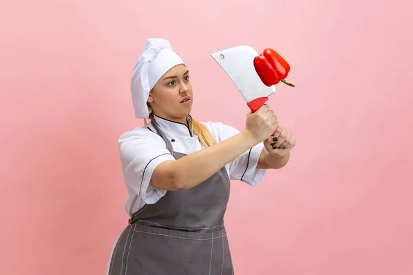 Kadın aşçının komik portresi, beyaz şapkalı şef ve pembe arka planda izole edilmiş mutfak önlüğü. Mutfak, meslek, iş, yemek, tat, restoran konsepti. — Stok fotoğraf