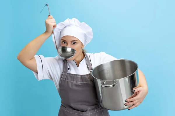 Ritratto di giovane donna caucasica, cuoca, cuoca in uniforme bianca con casseruola isolata su sfondo blu. Divertenti emozioni meme — Foto Stock