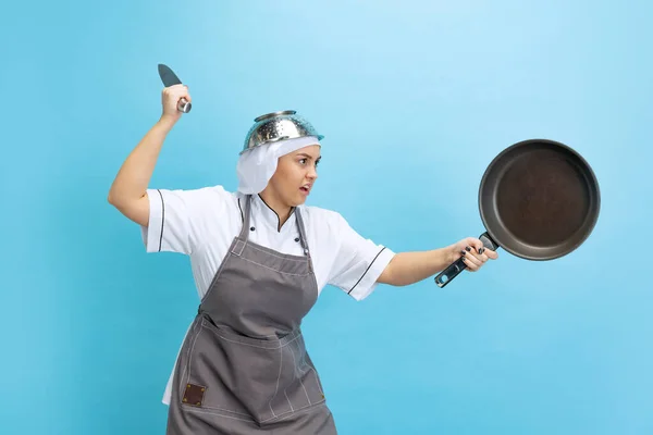 Cavaliere della cucina. Ritratto comico di bell'uomo, cuoca, cuoca in uniforme bianca che si diverte isolata su sfondo blu. Divertente meme emozioni concetto. — Foto Stock