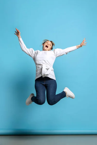 Full-length portrait of excited young girl jumping isolated on blue background. Concept of wow emotions, facial expressions, ad, sales — Stock Photo, Image