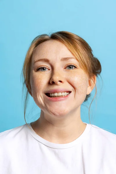 Primer plano joven chica bastante sonriente con pecas mirando a la cámara aislada en el fondo azul. Concepto de emociones, expresiones faciales — Foto de Stock