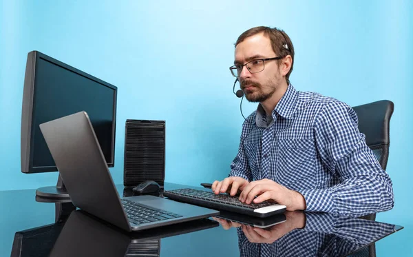 Portrait of concentrated man, call center operator working with laptop, answering online call isolated over blue background — Stock Photo, Image