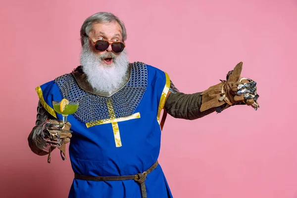 Porträt eines älteren Mannes mit grauem Bart, tapferer mittelalterlicher Krieger oder Ritter in gepanzerten Gewändern und Schwert isoliert auf rosa Hintergrund. Vergleich von Epochen, Geschichte, Festen — Stockfoto