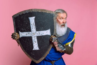 Yaşlı gri sakallı adamın portresi, cesur ortaçağ savaşçısı ya da pembe arka planda kılıçlı şövalye. Çağ, tarih, festival karşılaştırması