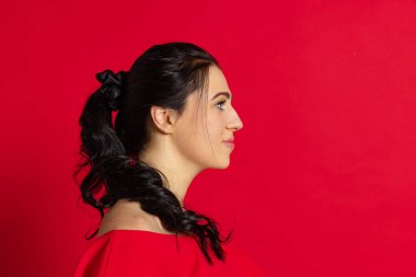 Profil görünümü. Kırmızı arka planda izole edilmiş uzun parlak siyah saçlı mutlu ve güzel bir kız. Duyguların kavramı, yüz ifadesi