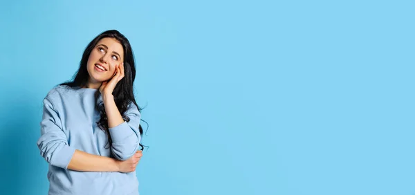 Portret van een jong mooi meisje met lang glanzend donker haar dat geïsoleerd poseert op een blauwe achtergrond. Concept van emoties, gezichtsuitdrukking — Stockfoto