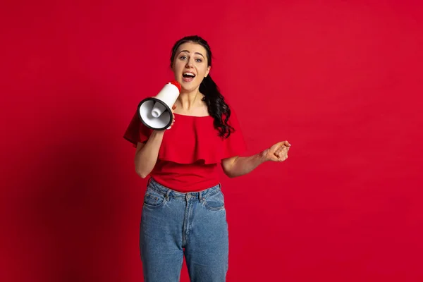 Studyjne ujęcie młodej wesołej dziewczyny noszącej luźne ubrania w stylu krzycząc na megafon odizolowany na czerwonym tle. Pojęcie emocji — Zdjęcie stockowe