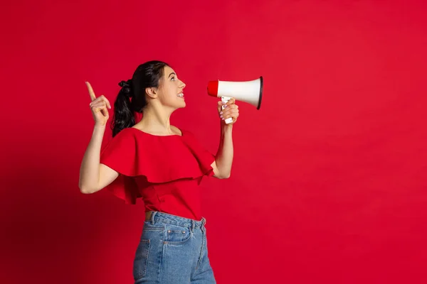 Foto de estudio de la joven chica alegre con ropa de estilo casual gritando a megáfono aislado sobre fondo rojo. Concepto de emociones — Foto de Stock