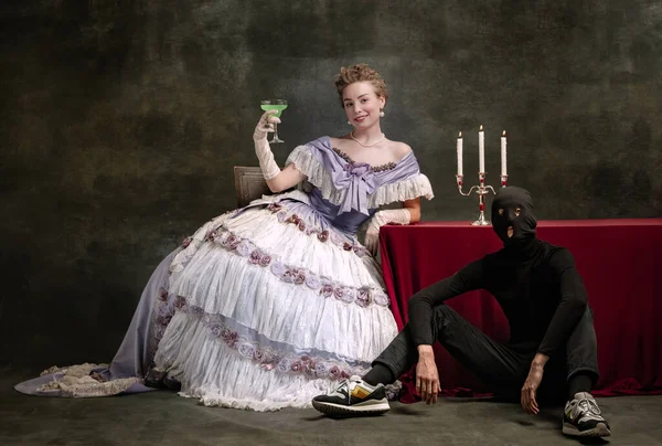 Young beautiful woman in image of medieval royal person in renaissance style dress and her page isolated on dark vintage background. — Stock Photo, Image