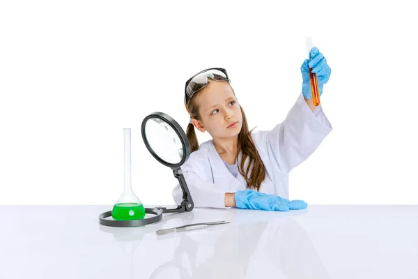 Portrait of little school girl, kid in white big gown as chemist, scientist doing experiment with multicolored chemical fluid in laboratory isolated on white background — Stock Photo, Image