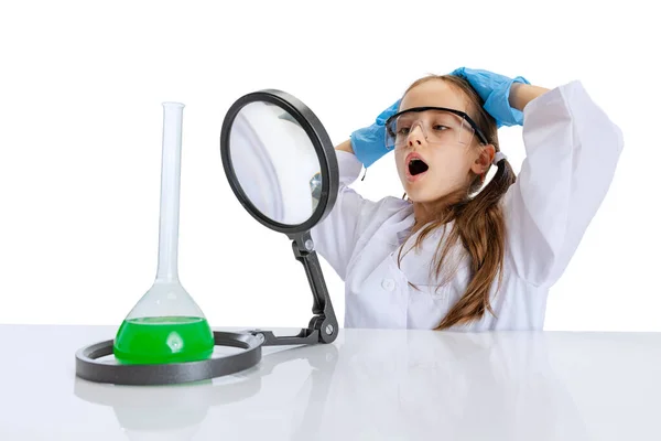 Zvědavé dítě, holčička, žák v bílých velkých šatech studuje, dělá experiment s mnohobarevnou chemickou tekutinou v chemii třídy izolované na bílém pozadí — Stock fotografie