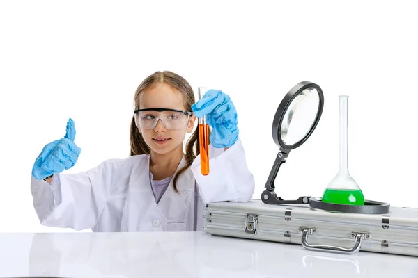 Curious child, little girl, pupil in white big gown studying, doing experiment with multicolored chemical fluid in chemistry class isolated on white background — Stock Photo, Image