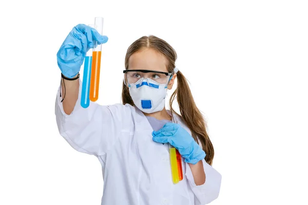 Στούντιο πλάνο του μικρού χαριτωμένο κορίτσι, παιδί σε λευκό μεγάλο φόρεμα ως χημικός, επιστήμονας κάνει πειράματα με χρωματιστά χημικά υγρά που απομονώνονται σε λευκό φόντο. Εκπαιδευτική έννοια — Φωτογραφία Αρχείου