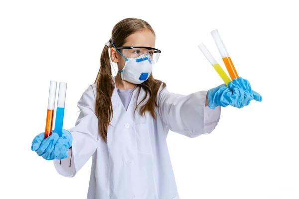 Studio shot of little cute girl, kid in white big gown as chemist, scientist doing experiment with colored chemical fluid isolated on white background. Education concept — Stock Photo, Image