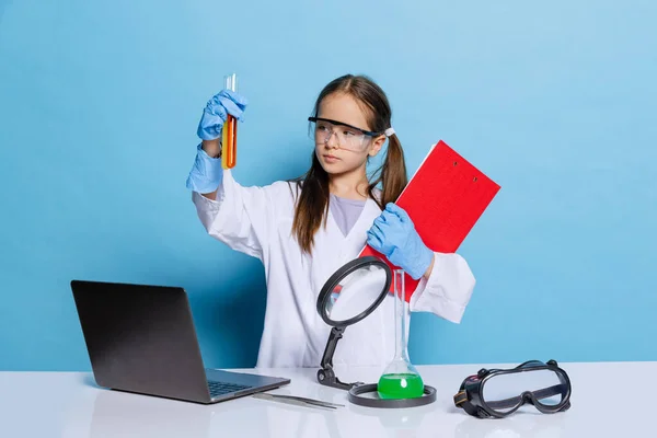 Portré kis iskolás lány, gyerek fehér nagy köpeny, mint vegyész, tudós kémiai berendezések, folyadék laboratóriumban elszigetelt kék háttér — Stock Fotó