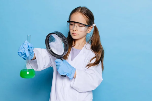 Portrait of little school girl, kid in white big gown as chemist, scientist chemical equipment, fluid in laboratory isolated on blue background — Stock Photo, Image