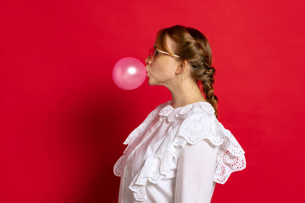 Profile view of young girl in white retro blouse posing isolated on red background. Concept of emotions, facial expressions