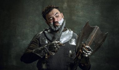 Ortaçağ savaşçısının komik portresi ya da kötü yaralanmış yüzlü şövalye eskitilmiş bir balta ile tıraş oluyor. Dönem, tarih, güzellik karşılaştırması