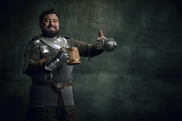 Ευτυχισμένος μεσαιωνικός πολεμιστής ή ιππότης με βρώμικο πληγωμένο πρόσωπο κρατώντας μια μεγάλη κούπα μπύρα απομονωμένη σε σκούρο vintage φόντο. Σύγκριση εποχών, ιστορία — Φωτογραφία Αρχείου