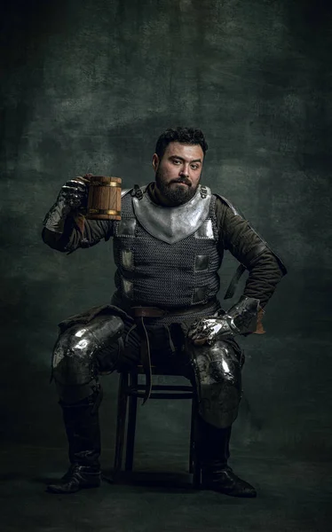 暗いヴィンテージの背景に隔離されたビールの大きなマグカップを保持汚れた負傷した顔を持つ幸せな中世の戦士や騎士。時代、歴史の比較 — ストック写真