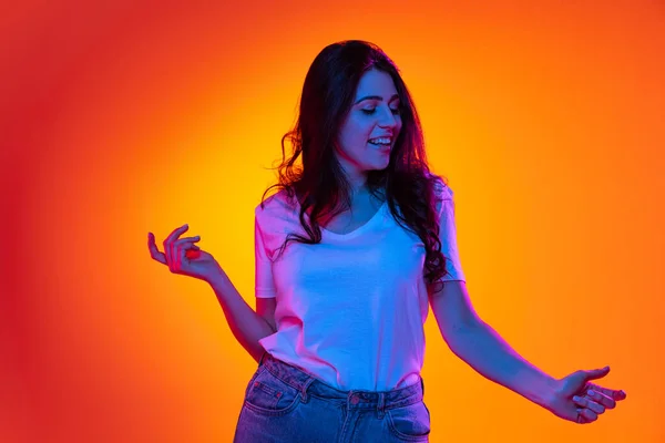 Jong mooi blank meisje met lang donker haar lachend en dansend geïsoleerd op oranje achtergrond in neon licht, filter. Concept van emoties, advertenties, verkoop — Stockfoto