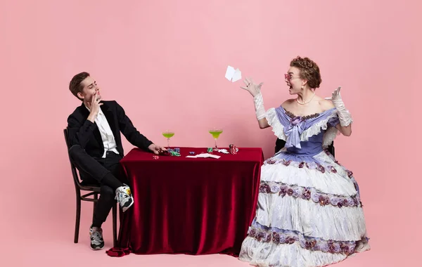Portrait of young beautiful woman in image of medieval royal person in evening dress with servant, page-boy playing isolated on pink background. Comparison of eras — Stock Photo, Image