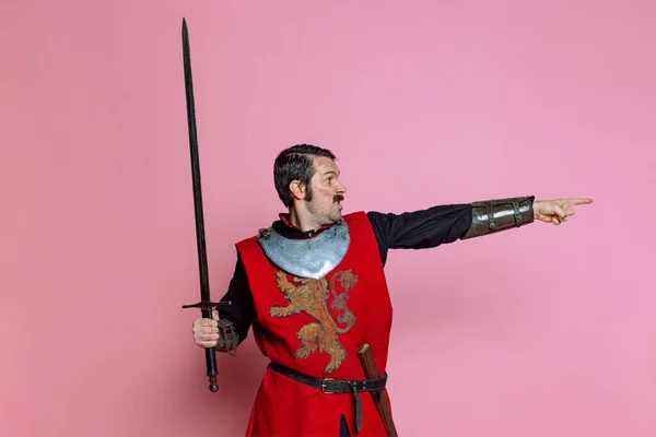 Komiczny portret średniowiecznego wojownika lub rycerza noszącego zbroję trzymającego duży miecz na różowym tle. Porównanie epok, historii — Zdjęcie stockowe