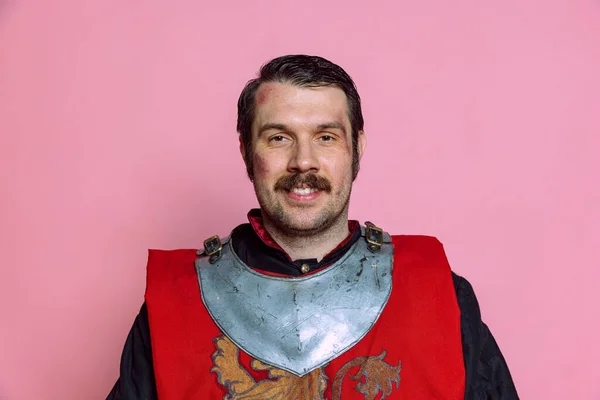 Un joven feliz, guerrero medieval o caballero vestido con armadura posando aislado sobre fondo rosa. Comparación de épocas, historia, emociones —  Fotos de Stock