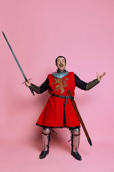 Um jovem, guerreiro medieval ou cavaleiro vestindo roupas de armadura posando isolado sobre fundo rosa. Comparação de eras, história, wow emoções — Fotografia de Stock