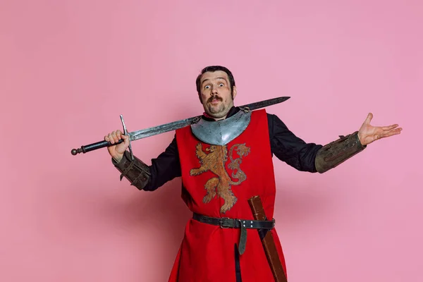 Um jovem, guerreiro medieval ou cavaleiro vestindo roupas de armadura posando isolado sobre fundo rosa. Comparação de eras, história, emoções — Fotografia de Stock
