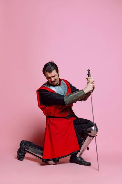 Κλάμα νεαρός άνδρας, μεσαιωνικός πολεμιστής ή ιππότης φορώντας ενδυμασία πανοπλία θέτουν απομονωμένη πάνω από ροζ φόντο. Σύγκριση εποχών, ιστορίας, συναισθημάτων — Φωτογραφία Αρχείου
