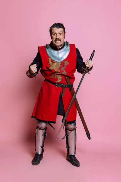 Um jovem, guerreiro medieval ou cavaleiro vestindo roupas de armadura posando isolado sobre fundo rosa. Comparação de eras, história, emoções — Fotografia de Stock