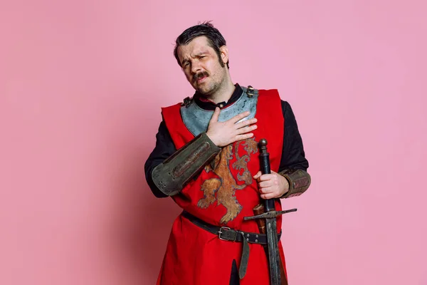 Jeden młody człowiek, średniowieczny wojownik lub rycerz ubrany w zbroję, pozujący na różowym tle. Porównanie epok, historii, emocji — Zdjęcie stockowe