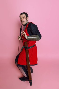 Korkunç adamın tam boy portresi, Ortaçağ savaşçısı ya da zırhlı şövalye, pembe stüdyo arka planında izole edilmiş kırmızı kostüm. Komik mim duyguları