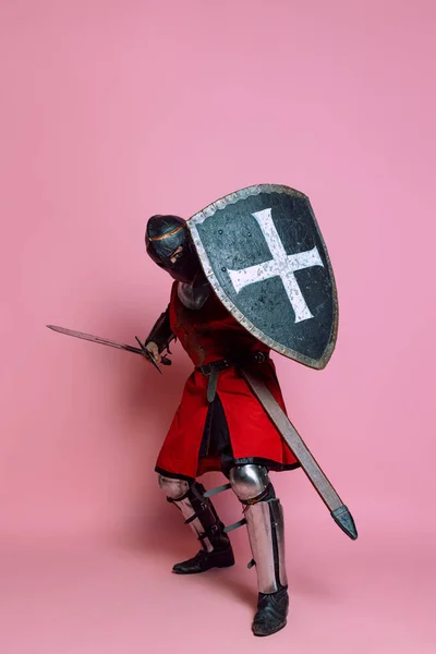 Retrato de guerrero medieval o caballero vestido con armadura que sostiene escudo y espada aislados sobre fondo rosa. Comparación de épocas, historia —  Fotos de Stock