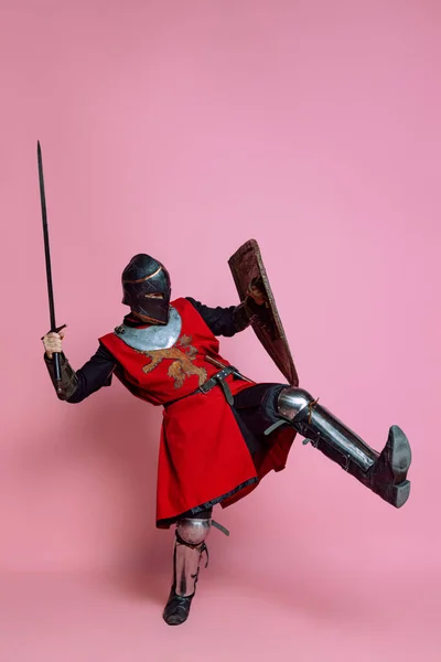 Portrét středověkého válečníka nebo rytíře v brnění oděvu držícího štít a meč izolovaný na růžovém pozadí. Porovnání období, historie — Stock fotografie