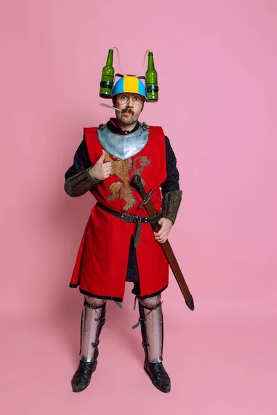 Ritratto a figura intera di uomo dall'aspetto divertente, guerriero medievale o cavaliere in casco da birra e armatura protettiva isolato su sfondo rosa studio — Foto Stock