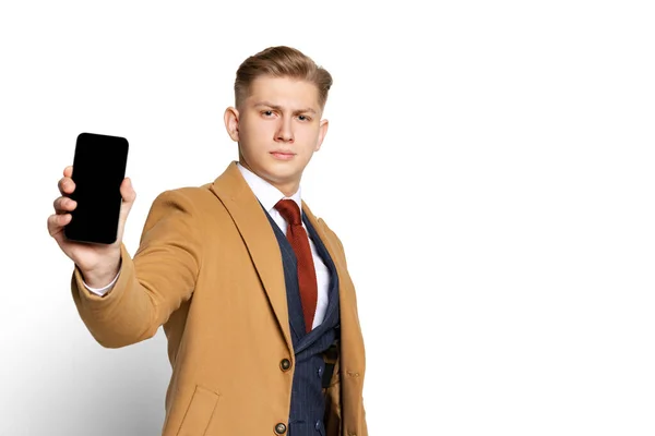 Portrét mladého podnikatele, studenta, elegantního muže v obleku a béžovém kabátě pomocí telefonu izolovaného na bílém pozadí studia. — Stock fotografie