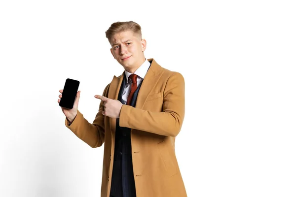 Muotokuva nuori liikemies, opiskelija, tyylikäs mies yllään puku ja beige takki puhelimella eristetty valkoinen studio tausta. — kuvapankkivalokuva