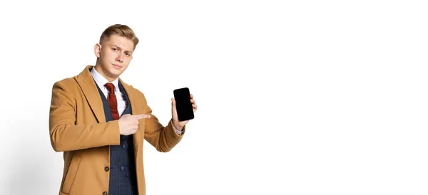 Porträtt av ung affärsman, student, elegant man bär kostym och beige rock med hjälp av telefon isolerad på vit studio bakgrund. — Stockfoto