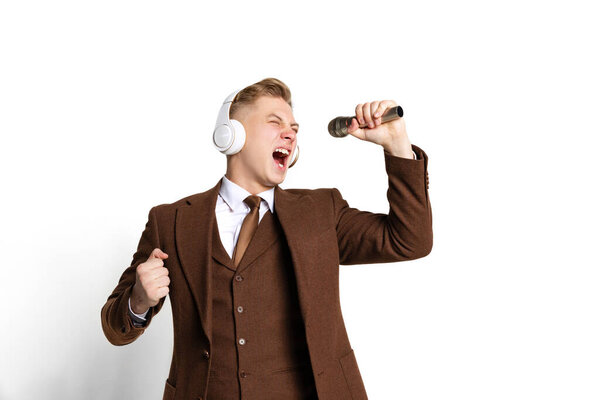 Emotional young man, student wearing suit of 80s, 70s fashion style in headphones isolated on white studio background. Beauty, fashion, music