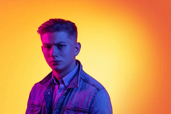 Closeup jovem homem bonito vestindo roupas casuais estilo jovem isolado no fundo laranja em luz de néon, filtro. Conceito de emoções, beleza, moda — Fotografia de Stock