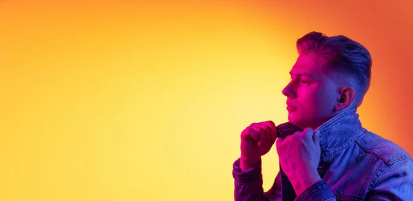 Flyer mit einem jungen gutaussehenden Mann in lässiger Jugendstilkleidung auf orangefarbenem Hintergrund in Neonlicht, Filter. Konzept von Emotionen, Schönheit, Mode — Stockfoto