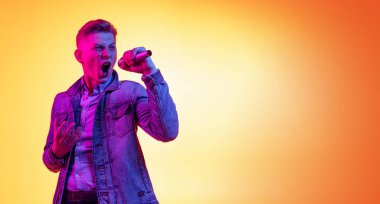 Duygusal, genç ve yakışıklı bir adam günlük kıyafetleriyle turuncu arka planda izole edilmiş, neon ışıklı, filtreli. Duygular, güzellik, moda kavramı