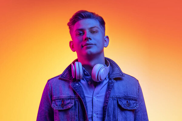 Портрет молодого красивого мужчины в повседневной молодежной одежде на оранжевом фоне в неоновом свете, фильтр. Концепция эмоций, красоты, моды