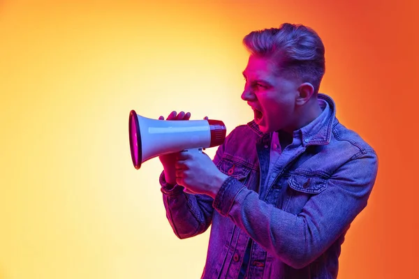 Screaming young handsome man in casual clothes isolated on orange background in neon light, filter. Concept of emotions, beauty, fashion — Stock Photo, Image