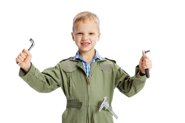 Porträt eines kleinen Jungen, eines niedlichen Kindes im Bild eines Automechanikers oder Installateurs in grüner Latzhose mit Arbeitswerkzeugen, die über weißem Studiohintergrund isoliert sind. Kindheit, Bildungskonzept — Stockfoto